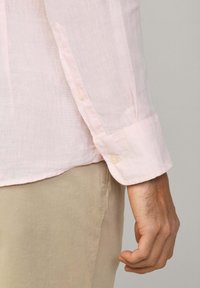 Camisa de lino de manga larga en rosa claro con puños abotonados, que presenta un acabado texturizado y un ajuste casual. El puño muestra un detalle de un solo botón.