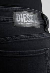 Černé džíny z denimu s výraznou ko ženou nášivkou s logem "DIESEL" na zadní straně, s viditelným prošíváním a hladkou, elegantní texturou.