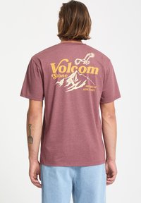 Bordeauxrotes T-Shirt mit einem grafischen Druck, der Berge, Vögel und "Volcom Stone" in Gelb zeigt. Kurze Ärmel und Rundhalsausschnitt.