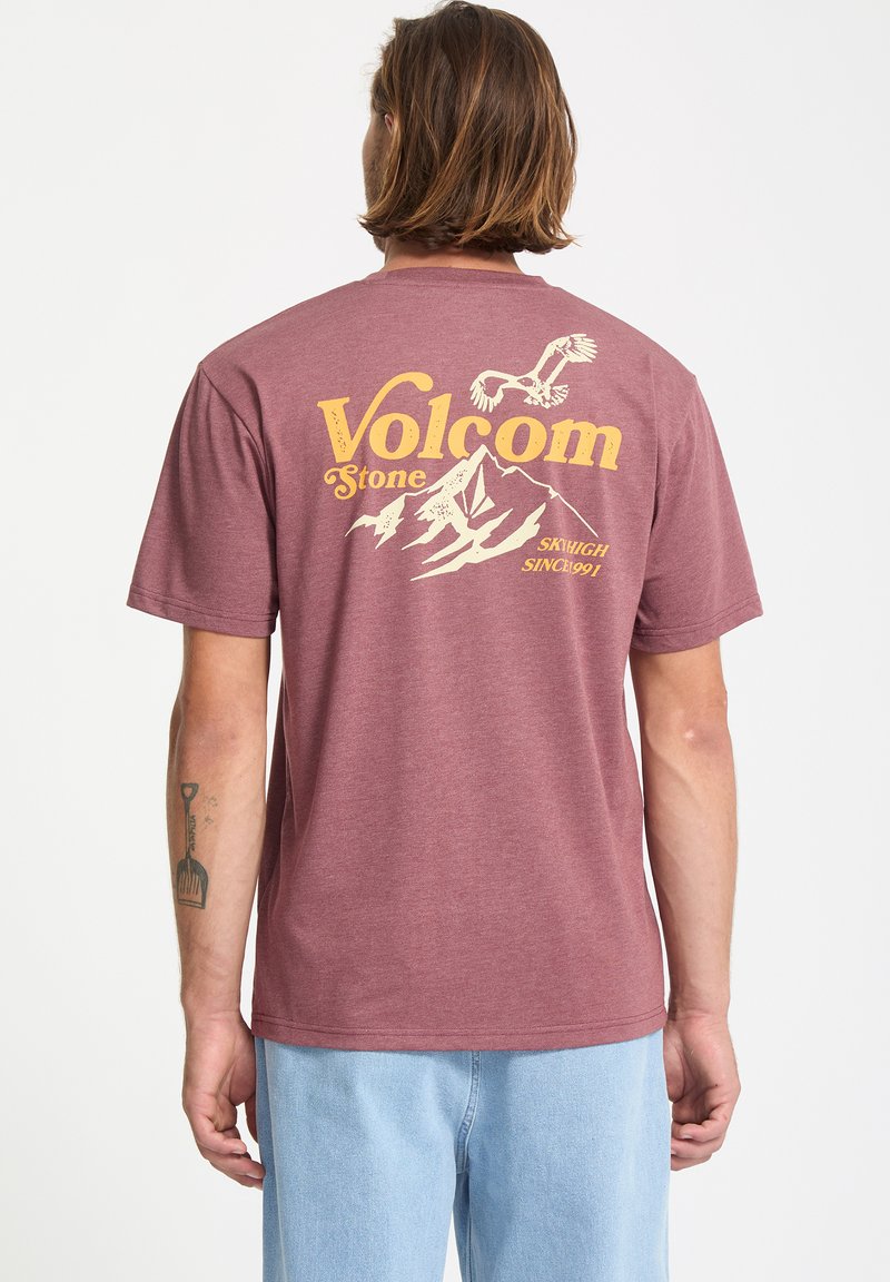 Bordeauxrotes T-Shirt mit einem grafischen Druck, der Berge, Vögel und "Volcom Stone" in Gelb zeigt. Kurze Ärmel und Rundhalsausschnitt.