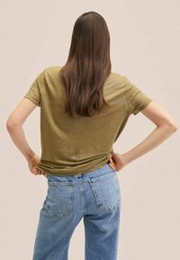 Olijfgroene t-shirt met korte mouwen gecombineerd met lichtblauwe spijkerbroek. Het shirt heeft een iets ruime pasvorm, met een eenvoudig ontwerp en een ronde hals.