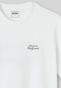 T-shirt en coton blanc avec un col rond et des manches courtes, ornée d'un texte brodé bordeaux "Rencontrez-moi sur le terrain de jeu" sur la poitrine.