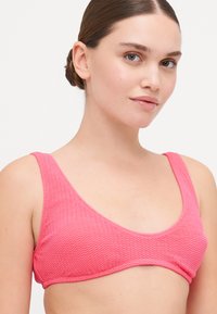 Haut de bikini rose avec un motif en zigzag texturé, des larges bretelles et un décolleté arrondi. Fabriqué dans un matériau flexible et extensible.