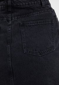 Jean en denim noir taille haute avec une texture lisse, doté d'une seule poche arrière et de coutures discrètes.