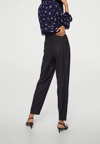 Blusa blu navy con un motivo rosa, abbinata a pantaloni neri a vita alta. I pantaloni presentano una vestibilità rilassata e un design su misura, completati da tacchi a strappo.