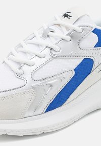 Adidași albi cu accente albastre și argintii, având materiale din plasă texturată și suede, elemente de design complexe și șireturi plate.