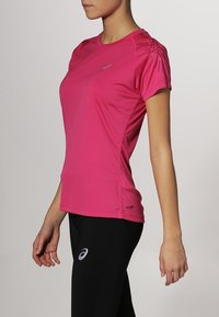 Tajt kortärmad träningsskjorta i starkt rosa, med axelaccenter och sportig design. Matchas med svarta leggings, minimal märkning synlig.