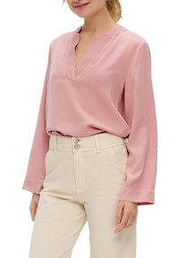 Blusa rosa a maniche lunghe con scollo a V e texture liscia, abbinata a pantaloni beige chiaro a vita alta con chiusura a doppio bottone.