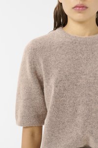 Strikkegenser i lys beige, med kort ermer, rund hals og en myk, lodden tekstur med subtile fargevariasjoner.