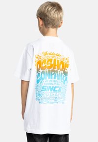 Vit bomullst-shirt med en färgglad grafik på baksidan med blå och gula texter, stjärnor och döskallar. Kort ärm och avslappnad passform.