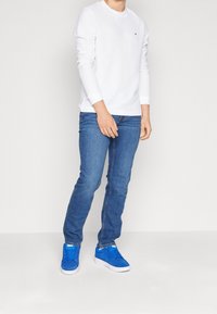 Vit långärmad skjorta, blå jeans och ljusblå sneakers med vita sulor. Enkelt design utan mönster eller märkbar hårdvara.