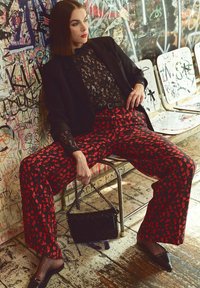 Zwarte kanten top gecombineerd met rode, gedessineerde wijde broek. Accessoires zijn onder andere een zwarte handtas met kettingriem en netkousen.