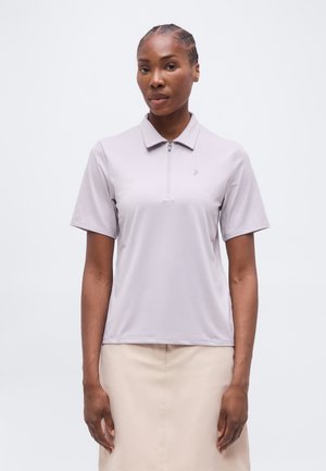 Γυναίκα με ανοιχτό γκρι κοντομάνικο πόλο πουκάμισο με φερμουάρ στον γιακά και μπεζ φούστα σε λευκό φόντο.