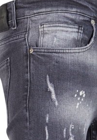 Gros plan sur la poche d'un jean en denim gris vieilli avec tissu décoloré et petites éclaboussures de peinture.