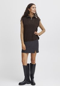 Brun udenærmet pullover sweater med lynlås krave, parret med en mørkegrå knælang nederdel med en frontslids, og høje sorte støvler.