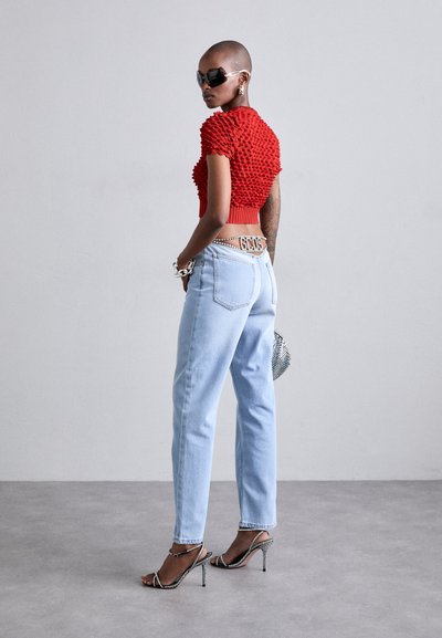 Rode gebreide crop top met textuurdesign, lichtblauwe high-waisted jeans en zilveren stiletto sandalen. Accessoires omvatten een zonnebril met tint en sieraden.