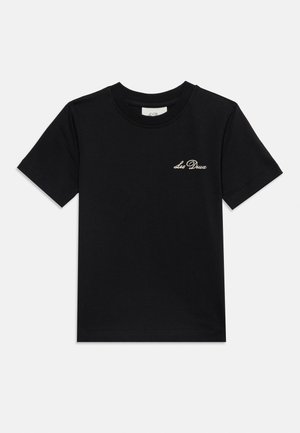 Sort T-shirt med korte ærmer med lille hvid kursiv "Les Deux" logo på venstre bryst mod en ensfarvet baggrund.