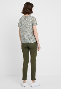 Tričko s krátkým rukávem a květinovým potiskem s výřezem na zádech, spárované s úzkými olivově zelenými kalhotami a bílými teniskami.