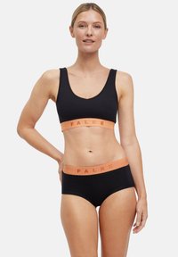 Zwarte sport-beha en bijpassende hipster onderbroek met een oranje elastische band met het "FALKE"-logo. Gladde stof, eenvoudig ontwerp.