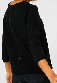 Czarna, strukturalna bluzka z rękawami o długości trzech czwarte, z okrągłym dekoltem i srebrnymi zatrzaskami wzdłuż pleców. Prosty i elegancki design.