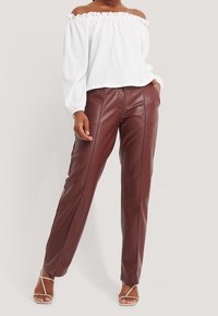 Weiße, strukturierte Bluse mit schulterfreiem Schnitt, kombiniert mit bordeauxroten, weiten Hosen aus Kunstleder, die vertikale Nähte aufweisen, sowie minimalistischen Sandalen.
