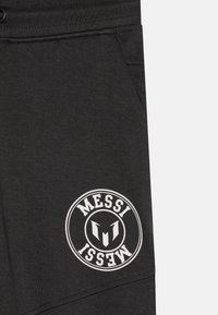 Fekete sportnadrág pamutból, bal combján egy kör alakú fehér logóval, rajta a "MESSI" felirattal és textúrás derékpánttal.