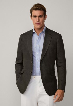 Dunkelgrauer Blazer mit taillierter Passform, einreihig, mit Reverskragen und zwei Knöpfen. Über einem hellblau gestreiften Hemd getragen.