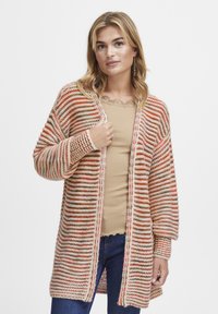 Stickad cardigan med horisontella ränder i orange, beigem och brunt. Långa ärmar, öppen framsida och mjuk textur. Bärs över en beige topp.