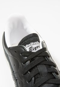 Sneaker nera in pelle con linguetta in rete, caratterizzata da lacci neri, una fodera interna bianca e un'etichetta del marchio con "Onitsuka Tiger" nella parte superiore.
