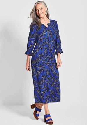 Blaues botanisches Maxikleid mit Dreiviertelärmeln, Knopfleiste, gerafftem Taillenbereich und Rüschensäumen. Kombiniert mit Absatzsandalen.