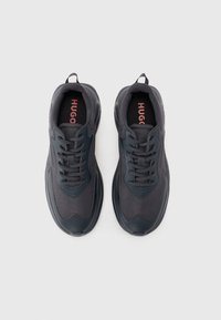 Dark gray athletic shoes with a smooth synthetic upper, textured fabric panels, and black laces. Features a red logo on the insole.