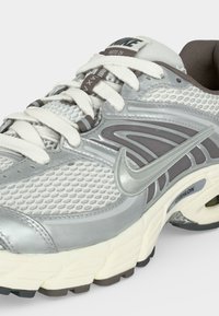 Ασημένιο και λευκό παπούτσι για τρέξιμο Nike με επάνω μέρος από δίχτυ, λευκά κορδόνια, επενδεδυμένη σόλα και εμφανές λογότυπο Nike στο πλάι.