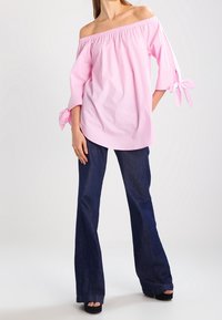 Top rosa chiaro a spalle scoperte con scollatura arricciata e maniche legate, abbinato a jeans in denim scuro svasati, indossato con sandali neri con zeppa.