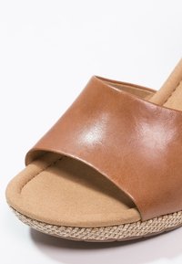 Gros plan d'une sandale beige à bout ouvert avec une large bride en cuir, une semelle intérieure rembourrée et un bord de semelle en jute tressée.