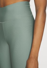 Högmidjade träningsleggings i en dämpad grön färg, med en slät textur, figurnära design och subtila sömdetaljer.