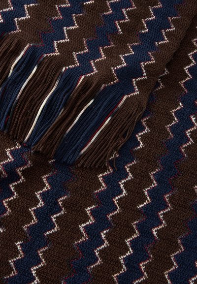 Tissu tricoté avec motif zigzag en marron foncé, bleu marine et blanc, avec un bord frangé comportant des brins de couleur alternée.
