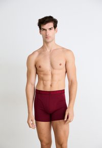 Boxer da uomo color marrone con una cintura logo nera. Tessuto morbido, design aderente e lunghezza fino a metà coscia per comfort e supporto.