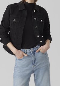 Black denim jacket with two front pockets, silver buttons, and a classic collar paired with light blue high-waisted jeans with a subtle faded texture.