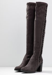 Botas por encima de la rodilla en ante gris oscuro con un alto tacón cuadrado y cordones decorativos en el lado exterior. Textura suave, diseño de puntera afilada.