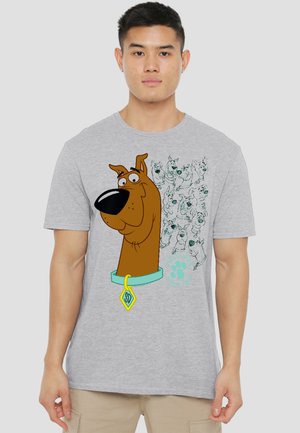 Young man wearing a gray t-shirt featuring a large cartoon Scooby-Doo face and smaller sketches of Scooby-Doo in various expressions.