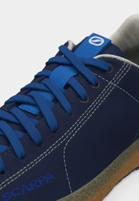 Παπούτσι σπορ σε ναυτικό μπλε με φανταχτερά μπλε κορδόνια, ενισχυμένη ραφή και υφή στη μπεζ σόλα.