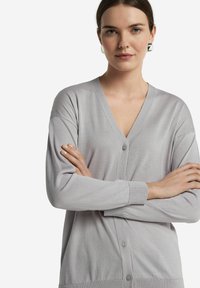 Ljusgrå cardigan med V-hals, knapplåsning fram och långa ärmar med ribbade manschetter. Mjuk struktur, avsedd för mångsidig lagerpåklädning.