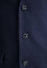 Marineblå ullfrakk med glatt tekstur, enkeltspent design og fire svarte knapper foran for lukking.