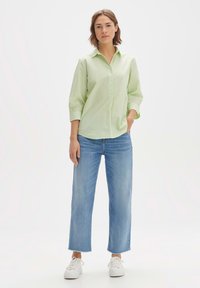 Camicia verde chiaro con colletto e maniche a tre quarti, abbinata a jeans a gamba larga blu chiaro e sneakers bianche.