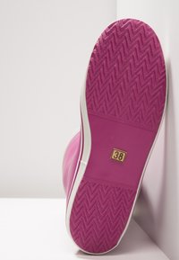 Rosa gummiskosula med texturerat zigzag-mönster, vit kant och storleksmärkning 38. Platt och designad för grepp.