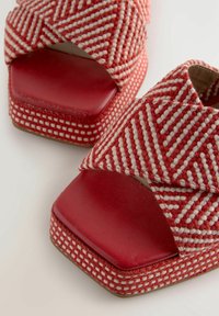 Sandales rouges avec des larges sangles tissées arborant un motif zigzag blanc et des bouts carrés sur un fond blanc.
