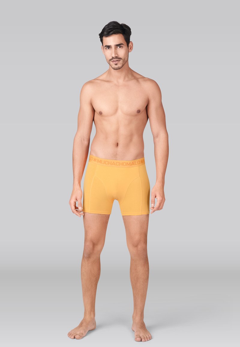Boxer en coton jaune avec une ceinture douce arborant la marque "MUCHACHO MALO". Texture lisse et coupe ajustée.