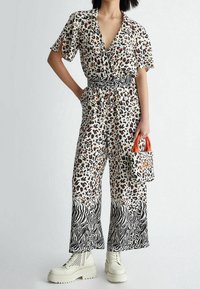 Leopard print jumpsuit with short sleeves, a deep V-neck, elastic waistband, zebra-patterned accents, paired with a small orange-handled bag.