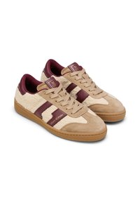 Beige sneakers met een textuurzijde in roomkleur, bordeaux accenten en een gouden logo. Heeft een vetersluiting en rubberen zool, en combineert materialen en stijl.