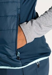 Marineblauer isolierter Jackett mit einer mit Reißverschluss versehenen Tasche; graue Langarminnenschicht sichtbar; mit hellblauen Akzenten am Saum und Reißverschluss.